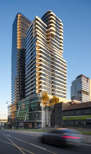Dramatic street-level view of two modern residential towers with curved forms; a black car with motion blur speeds past the base.
